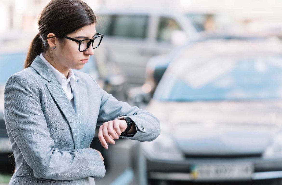 Femme d'affaires regardant sa montre près d'une voiture, illustrant la souscription rapide d'une assurance temporaire 30 jours.
